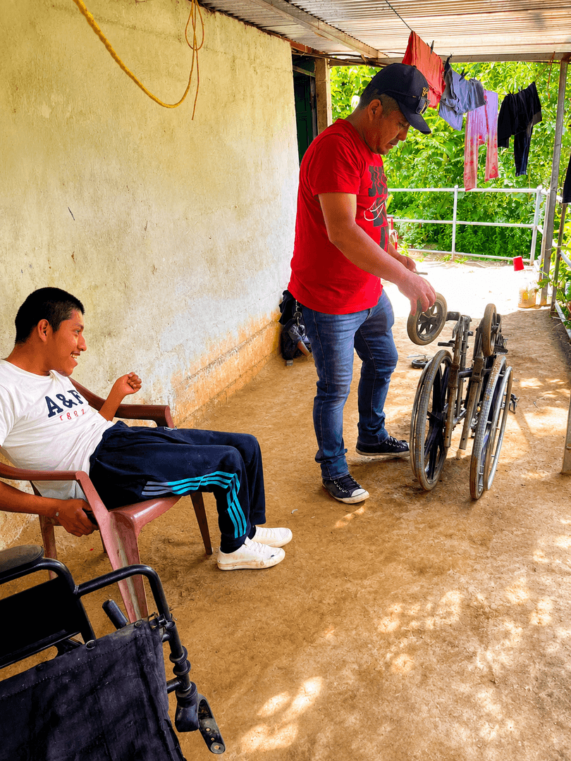 Un técnico ajusta una silla de ruedas en el corredor de la casa de un beneficiario.